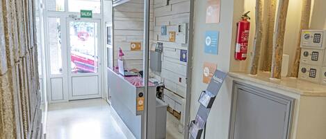Zona de recepción de un hotel con un mostrador, un extintor y carteles informativos en la pared.