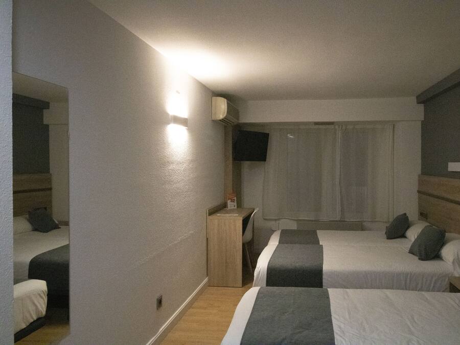 Habitación de hotel con dos camas, un escritorio, un televisor y una ventana con cortinas.