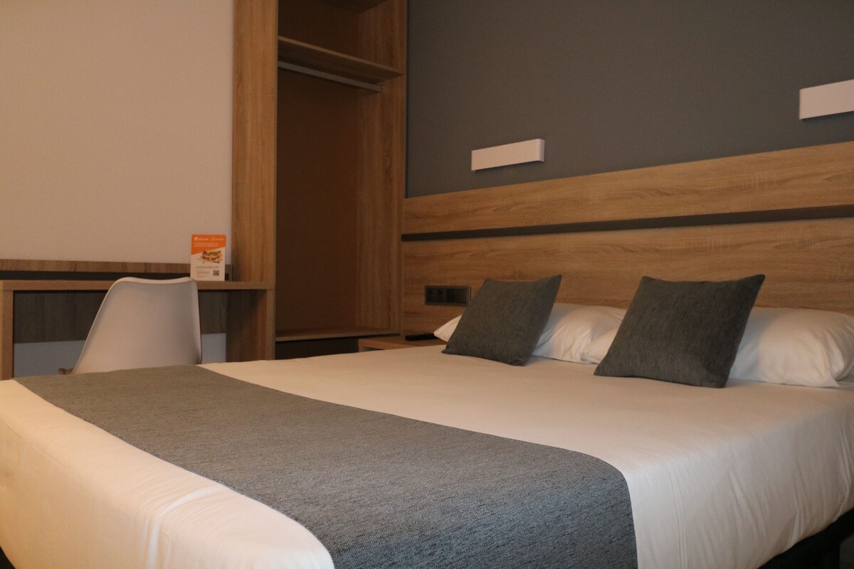Een hotelkamer met een groot bed, een houten hoofdeinde, een bureau met stoel en een kledingkast.