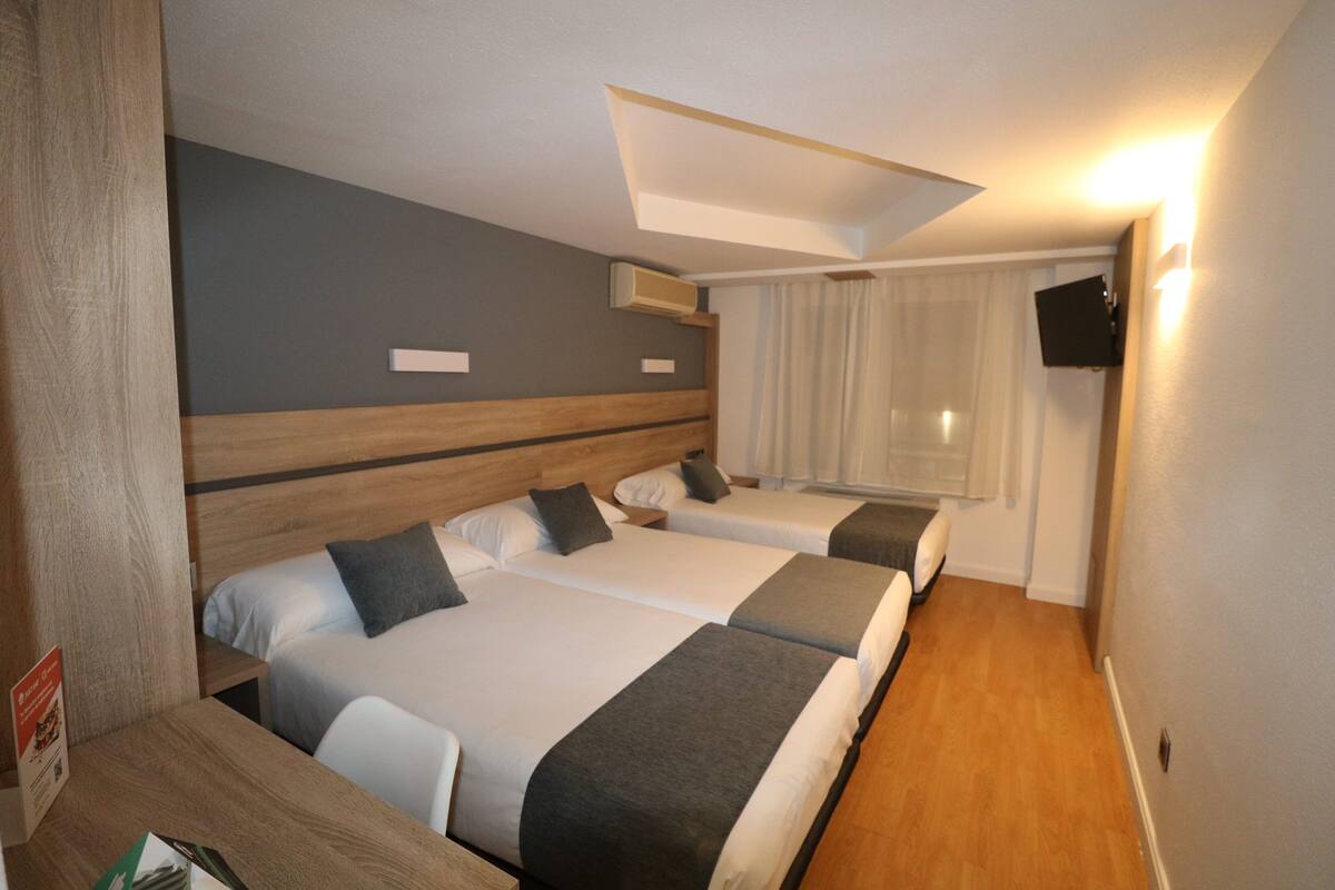 Ein Hotelzimmer mit zwei Betten, einem Holzkopfende, einem Flachbildfernseher und einem Fenster mit Vorhängen.