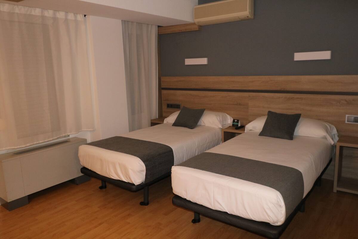 Ein Hotelzimmer mit zwei Einzelbetten, einem Holzkopfteil, einem Nachttisch mit Lampe und einem Vorhangfenster.