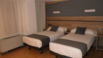Habitación de hotel con dos camas individuales, cabecera de madera, mesita de noche con lámpara y ventana con cortinas.