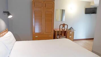 A bedroom with a bed, wooden wardrobe, desk, chair, and a TV mounted on the wall.