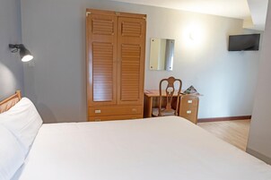 Un dormitorio con cama, armario de madera, escritorio, silla y televisor montado en la pared.