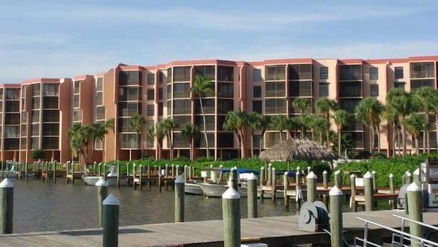 Un hôtel situé au bord de l’eau, doté de nombreux balcons, d’une zone avec un quai et de palmiers.