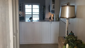 Eine Küche mit weißen Schränken, einem schwarzen Teppich und einer Holzkommode mit einer Lampe.