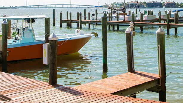 Eine Holzsteg ragt in ruhiges Wasser, ein Boot ist am Ende vertäut. Im Hintergrund ist eine Brücke über dem Wasser zu sehen.