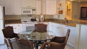 A kitchen with white cabinets, a microwave, stove, and a glass dining table with chairs. - Riverside B407 (Marco Island)