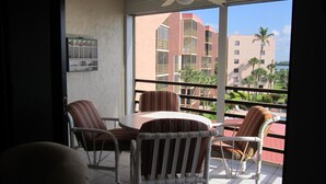A balcony with a table and chairs, a ceiling fan, and a view of buildings and palm trees. - Riverside B407 (Marco Island)