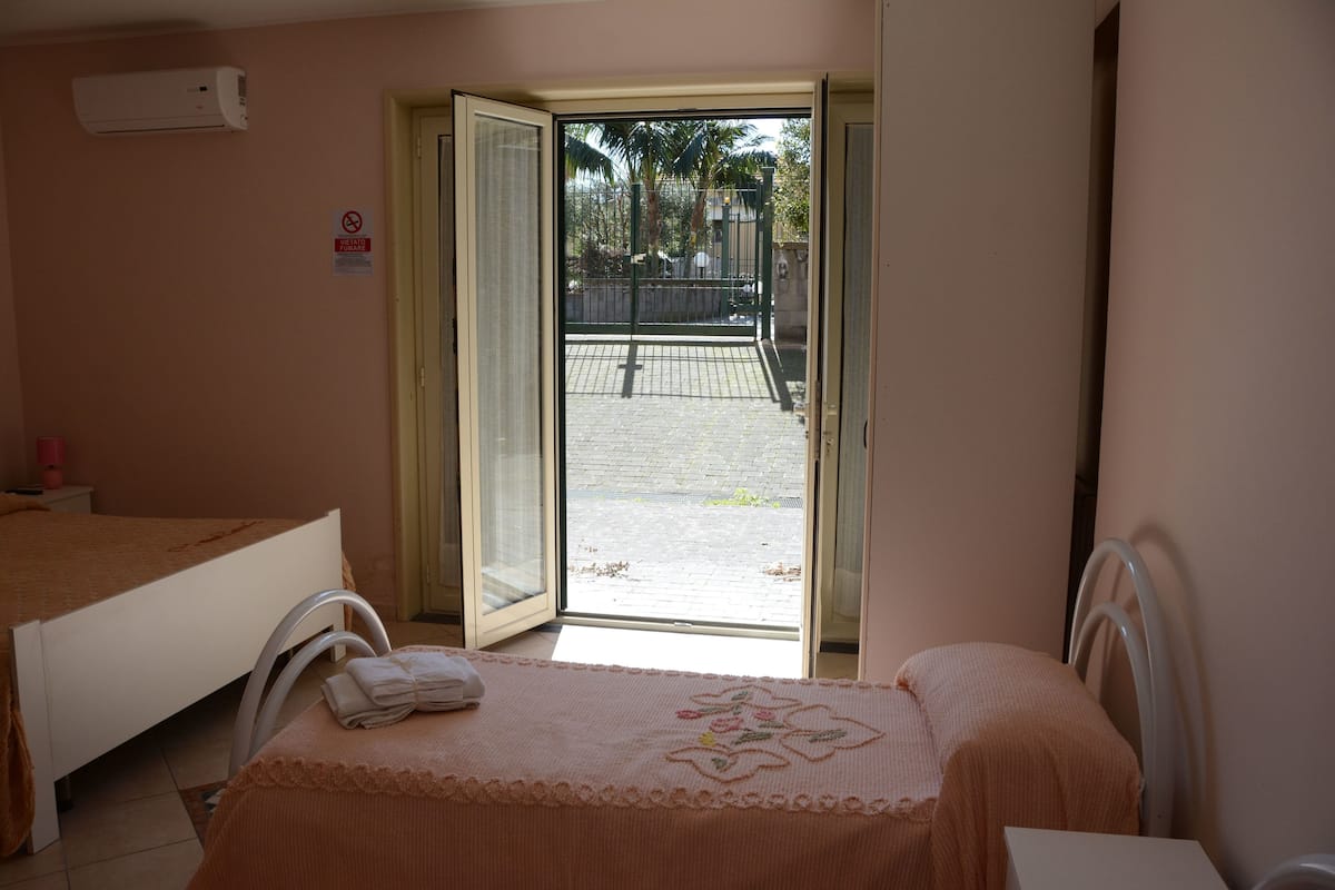 Habitación de hotel con dos camas, una ventana que da a vistas exteriores y una puerta que conduce a un balcón.