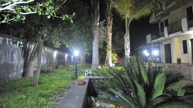Un espacio al aire libre de noche con un sendero, palmeras y un edificio con balcones.