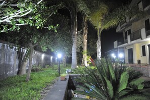 A nighttime outdoor area with a pathway, palm trees, and a building with balconies. - Villa San Leonardo (Mascali)