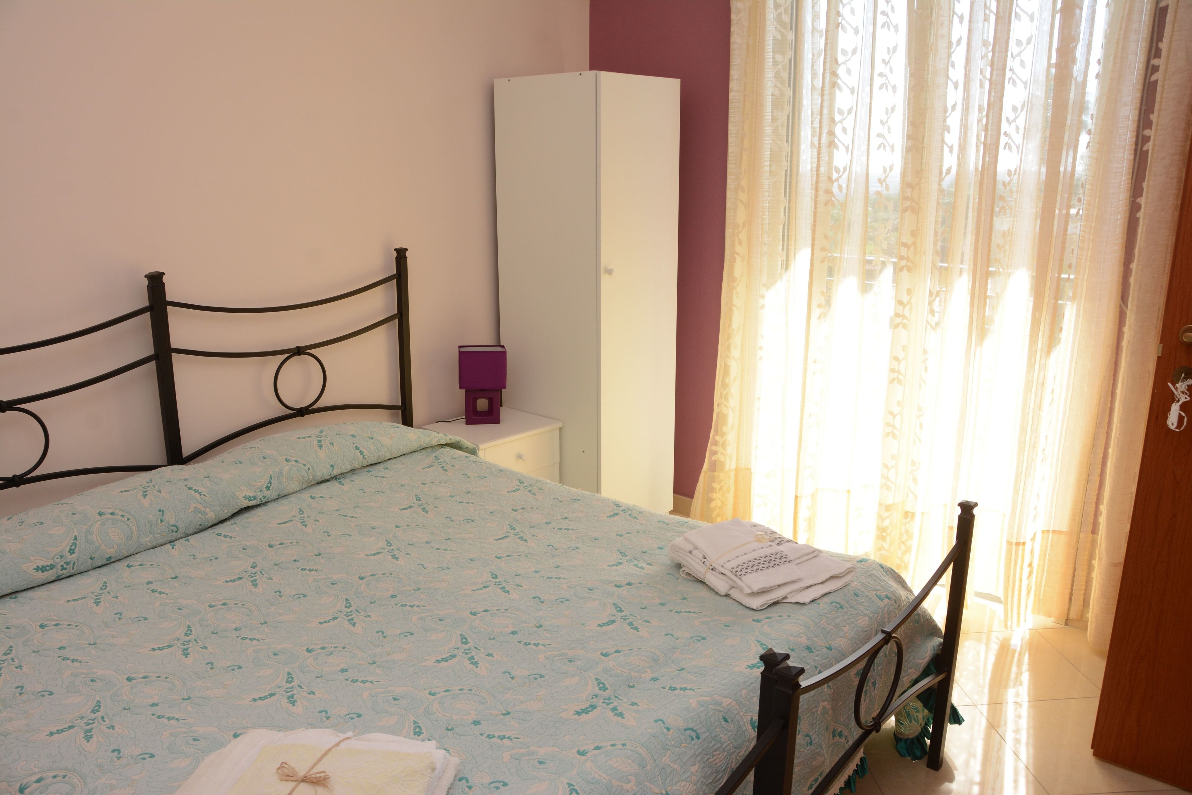 Une chambre à coucher comprenant un lit, une armoire, une table de chevet et une fenêtre avec des rideaux.