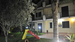 Un patio con un parque infantil, palmeras y un edificio con balcones y puertas.
