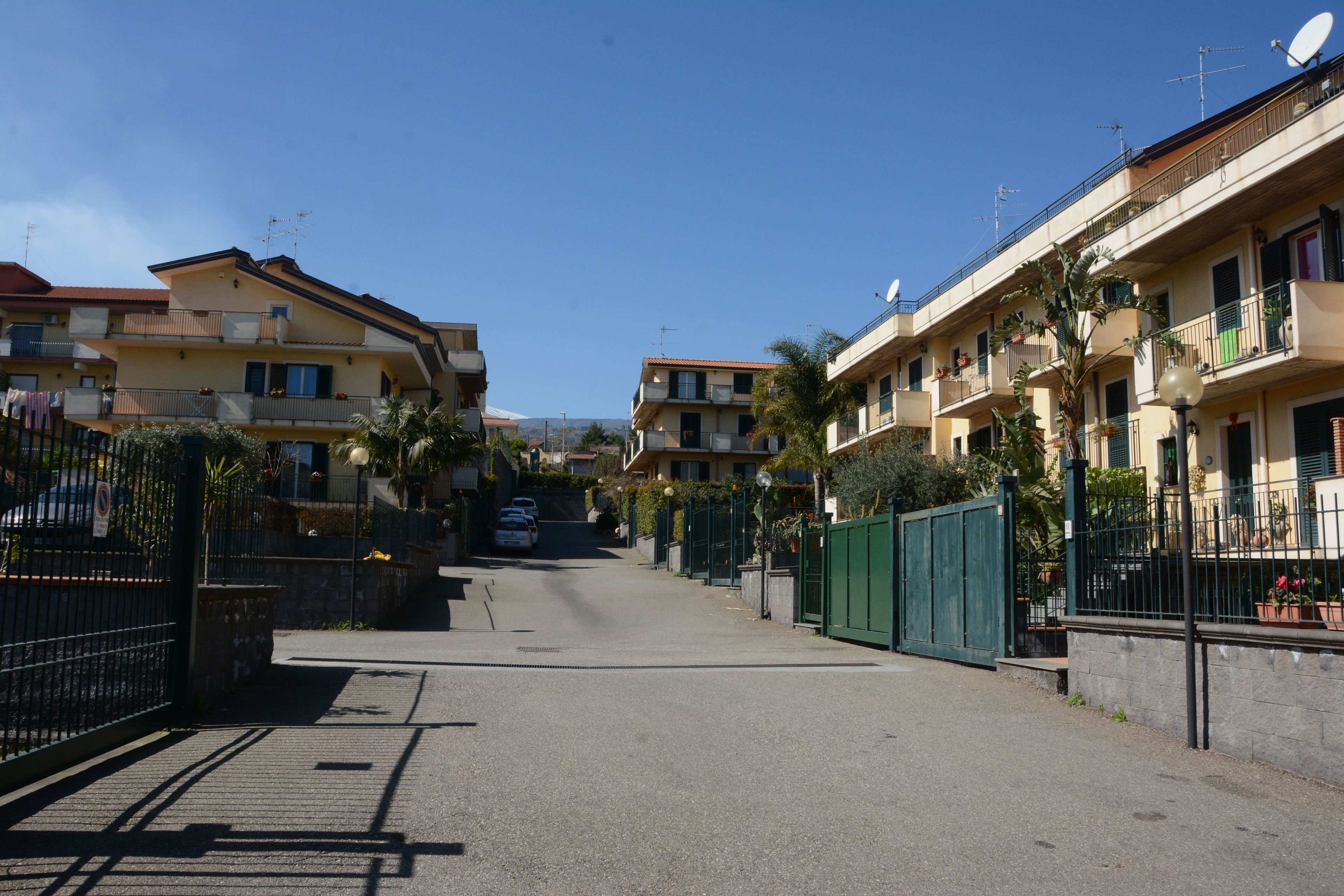 A residential street with apartment buildings on both sides, featuring balconies, satellite dishes, and a clear sky.