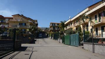 A residential street with apartment buildings on both sides, featuring balconies, satellite dishes, and a clear sky.