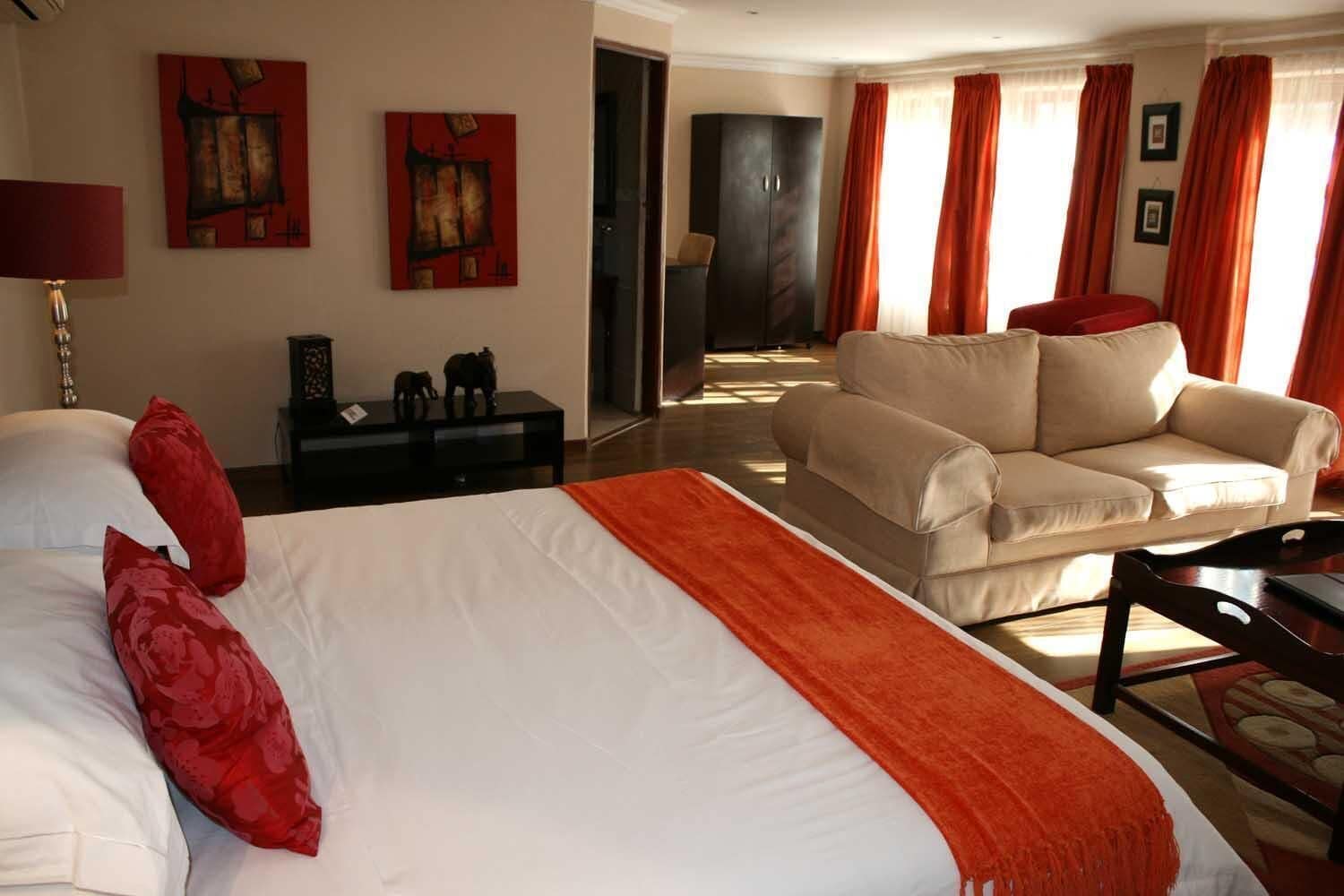 A hotel room with a large bed, a sofa, a desk, and two paintings on the wall.