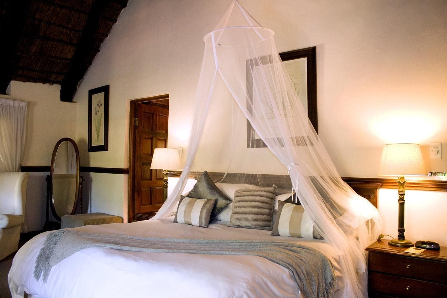 Un dormitorio con cama a dosel, puerta de madera, espejo y lámparas de noche.