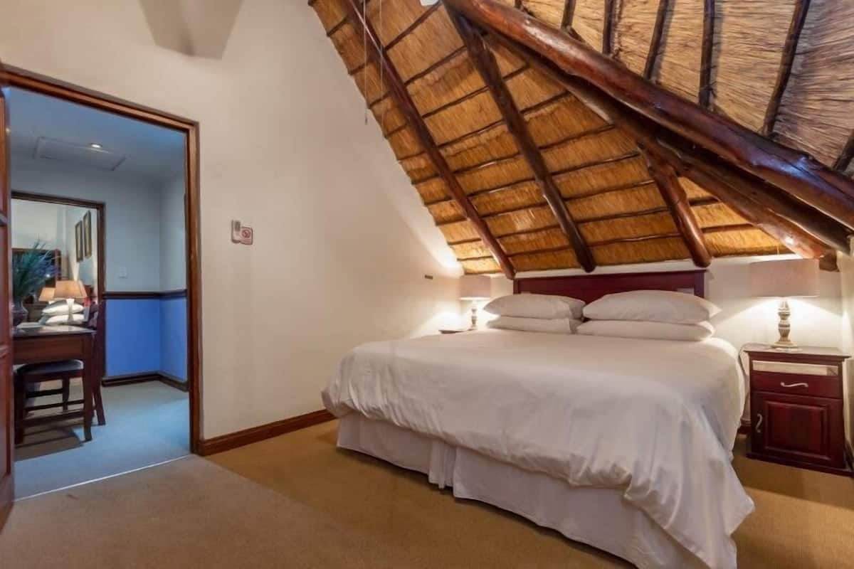 Un dormitorio con techo inclinado, una cama con ropa de cama blanca, una mesita de noche y un escritorio con silla.