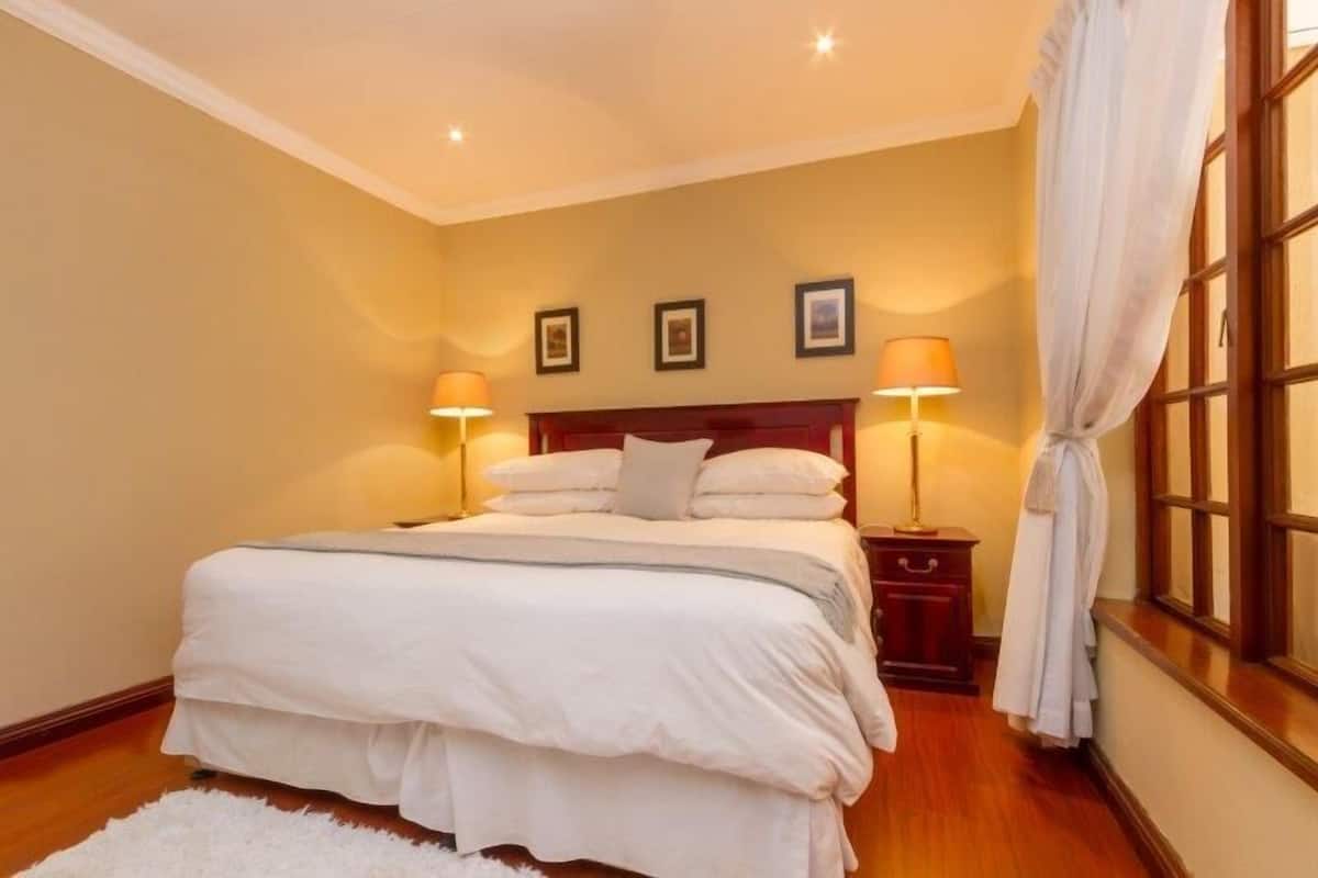 Un dormitorio ordenado con una cama grande, dos mesitas de noche con lámparas y una ventana con cortinas.