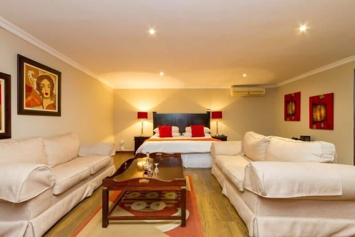 Una habitación de hotel con una cama, dos sofás blancos, una mesa de centro de madera y obras de arte en las paredes.
