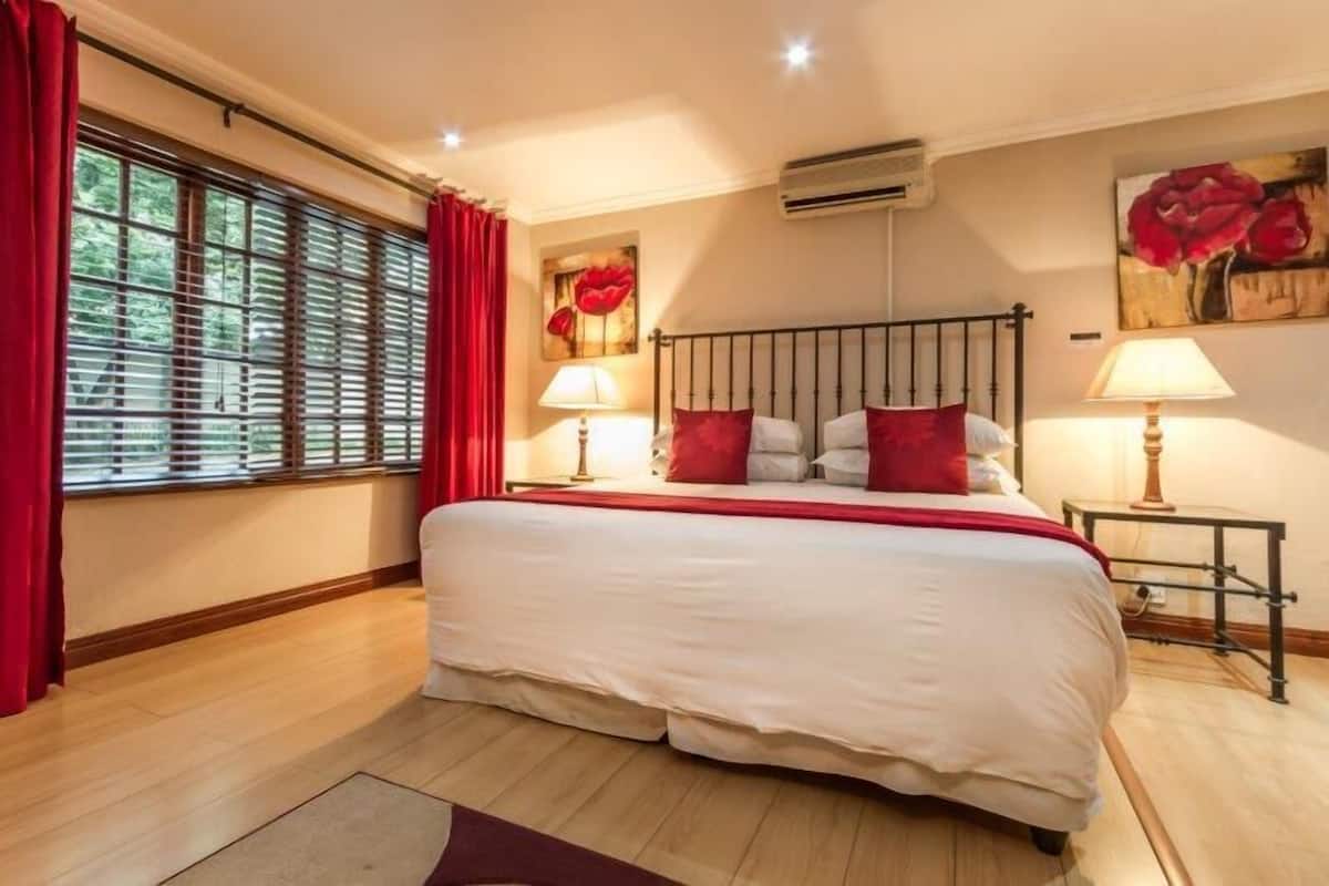 Un dormitorio con una cama grande, cortinas rojas, dos lámparas de noche y un cuadro de flores rojas en la pared.