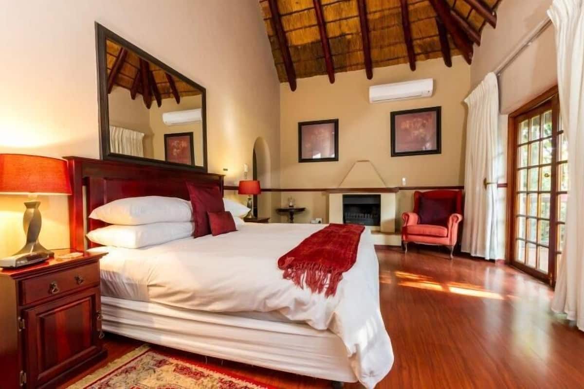 Un dormitorio espacioso con una cama grande, techo de madera, chimenea y vistas por una ventana.