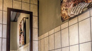 A bathroom with a tiled wall, a mirror, and a metal drying rack. - Rainforest Boutique Camp (Krugersdorp)