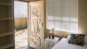 A bedroom with a bed, bedside table, lamp, and a door leading to an outdoor area. - Rainforest Boutique Camp (Krugersdorp)