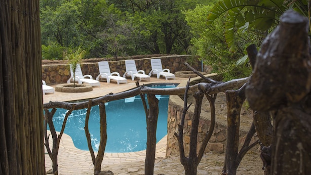 A pool area with white lounge chairs and a stone wall. - Rainforest Boutique Camp (Krugersdorp)