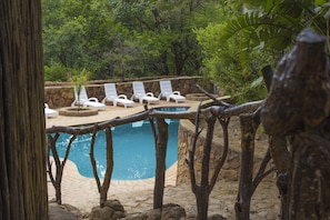 A pool area with white lounge chairs and a stone wall. - Rainforest Boutique Camp (Krugersdorp)