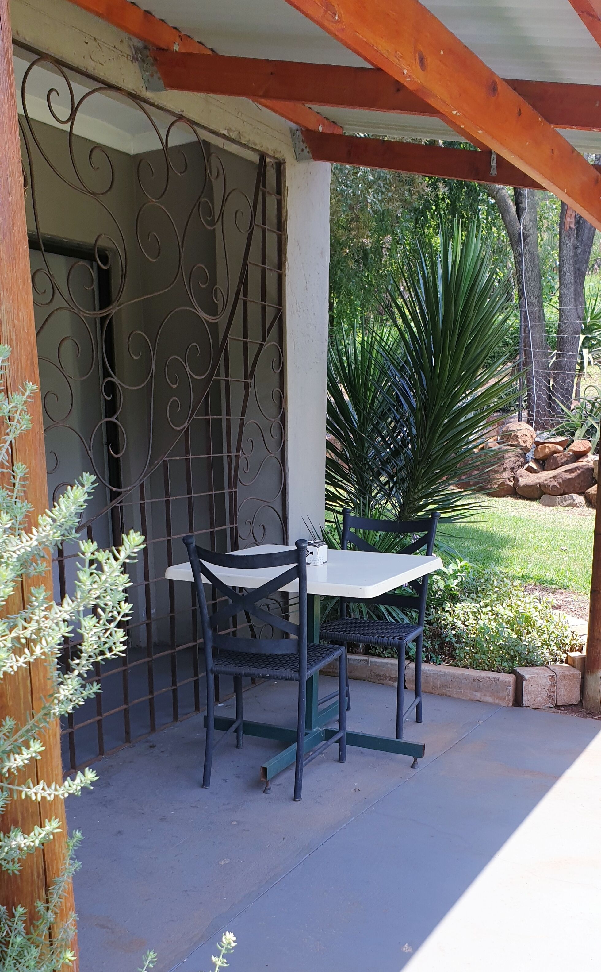 A patio with a table and chairs, a metal gate, and a garden with plants and a tree.