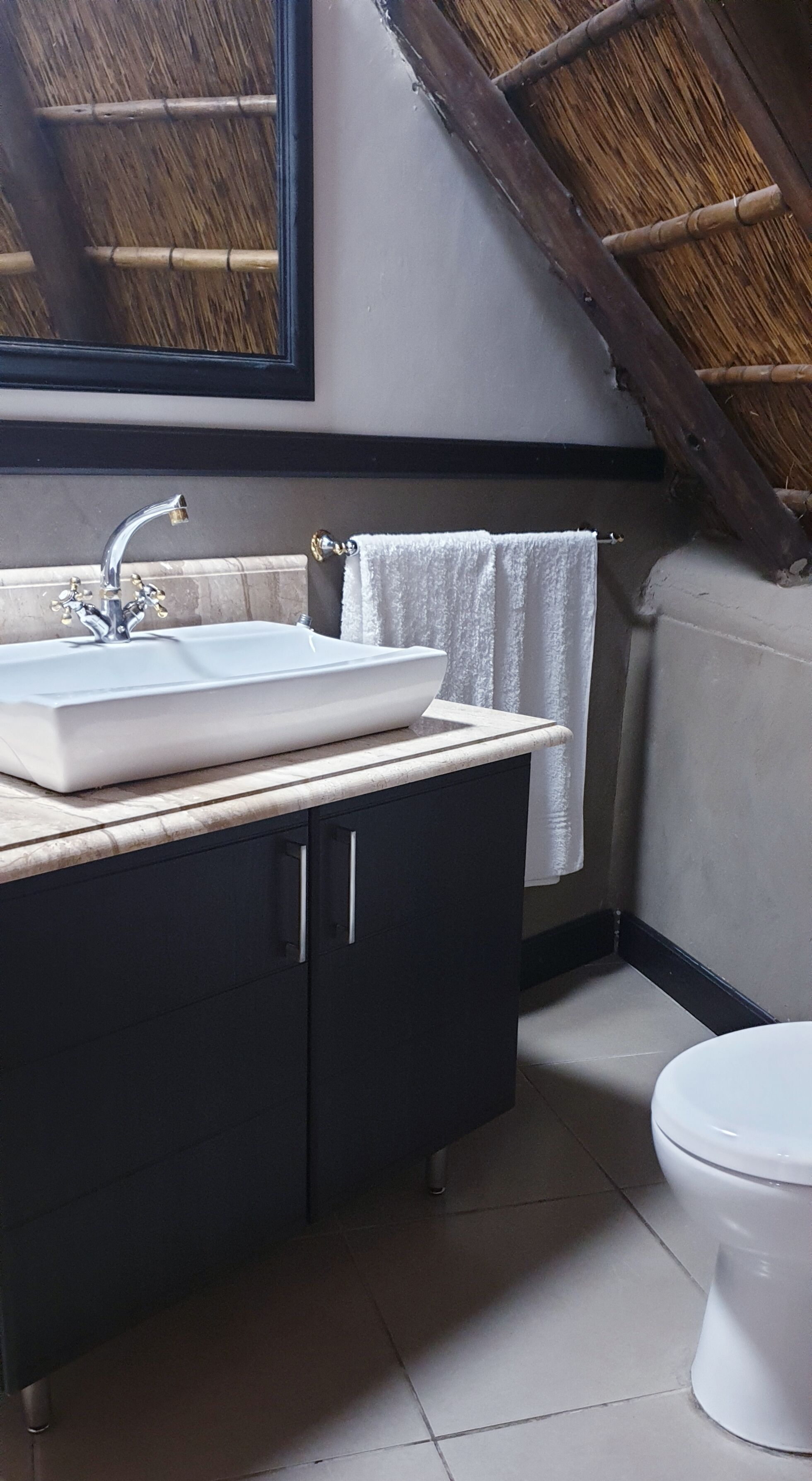 A bathroom with a white sink, dark cabinets, a white toilet, and a wooden ceiling.