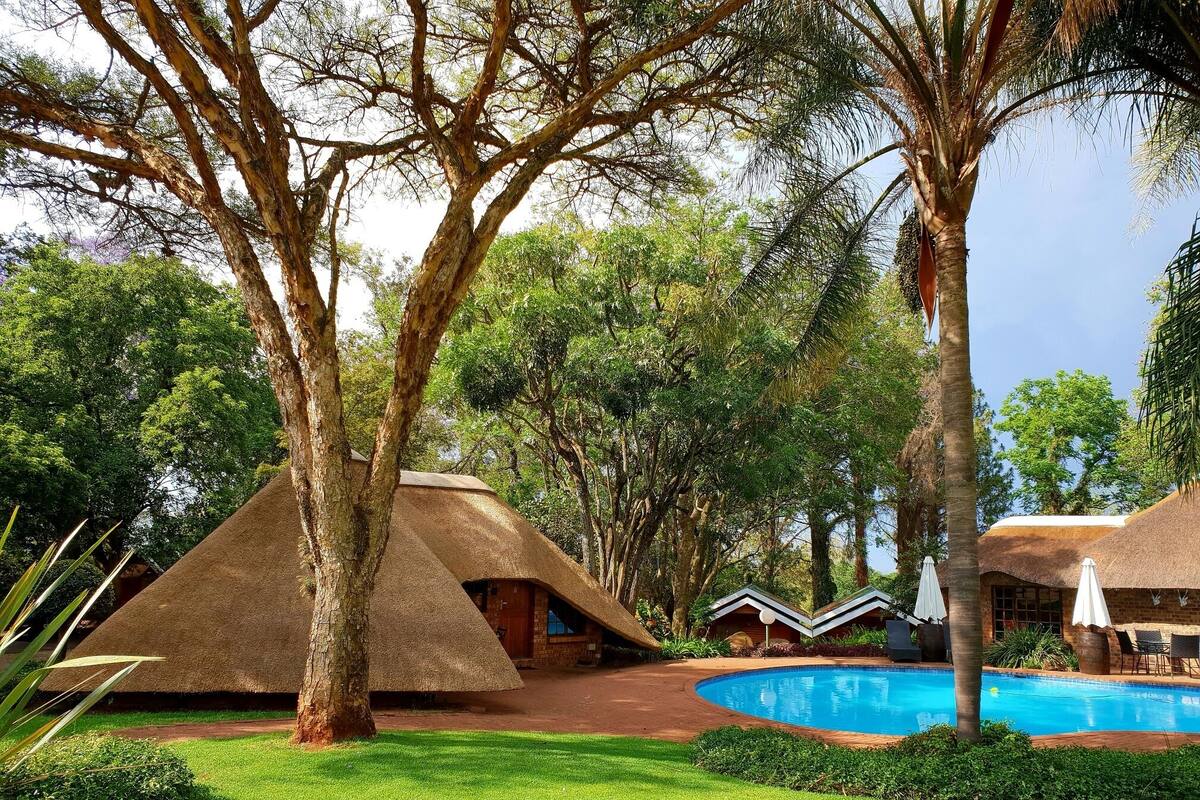 Um resort com cabanas de telhado de palha, piscina e vegetação exuberante.