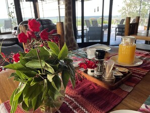 Comedor con una mesa dispuesta para dos, destacando un centro de mesa floral rojo, una jarrón de vidrio y condimentos.