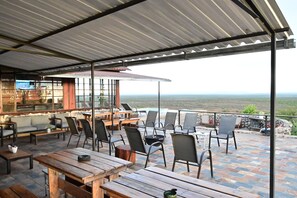 Un patio al aire libre con mesas y sillas de madera, una zona de bar y vistas al océano.