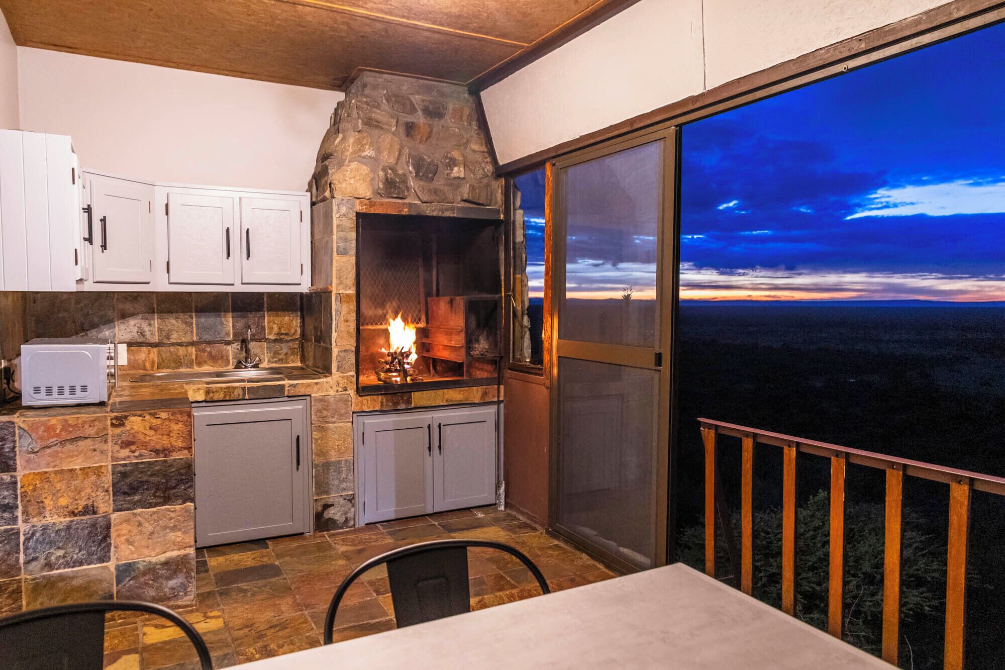 Una cocina con chimenea de piedra, armarios blancos y vistas del paisaje a través de un ventanal.