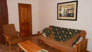 A living room with a wooden sofa, a wooden armchair, a wooden coffee table, and a framed picture on the wall. - Red Mountain House (Clarens)
