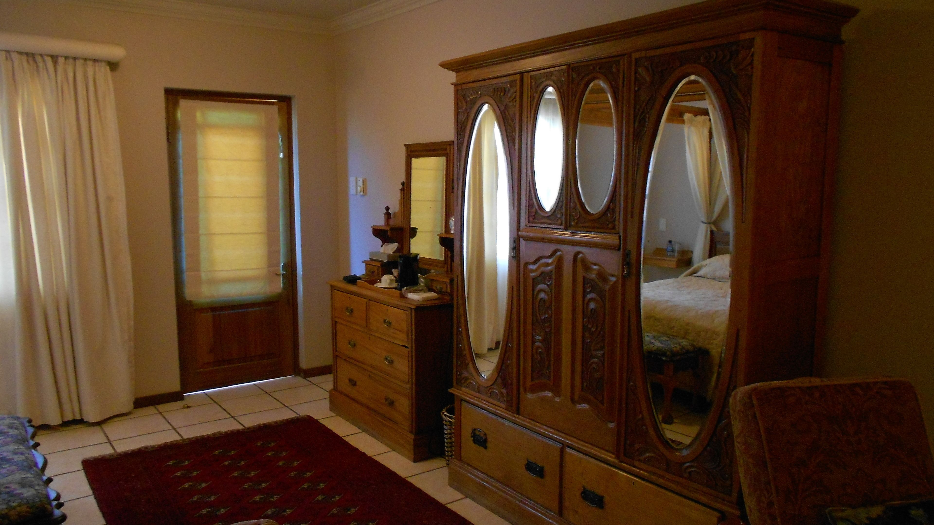 A bedroom with a wooden wardrobe, a bed, a dresser, and a mirror.