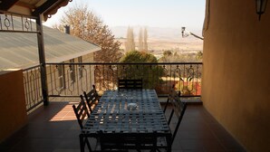 A balcony with a table and chairs, a view of trees and distant hills, and a metal railing. - Red Mountain House (Clarens)