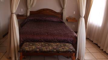 A bed with a wooden headboard, a bench at the foot of the bed, and curtains on the windows.