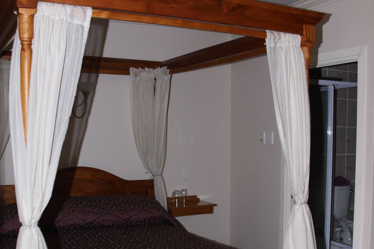 A four-poster bed with white drapes, a wooden headboard, and a purple bedspread.