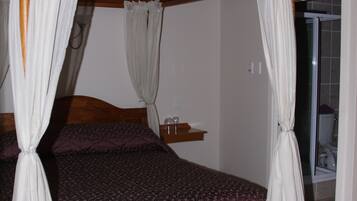 Un lit à baldaquin avec des rideaux blancs, une tête de lit en bois et une couvre-lit violette.