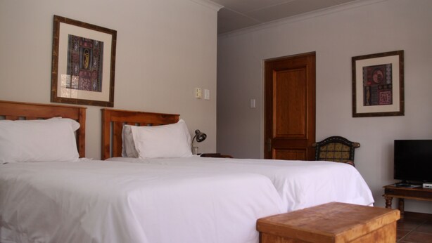 A bedroom with a large bed, wooden headboard, a wooden nightstand, a television, and two framed pictures on the wall. - Red Mountain House (Clarens)