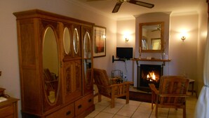 A living room with a large wooden cabinet, two armchairs, a television, and a fireplace. - Red Mountain House (Clarens)
