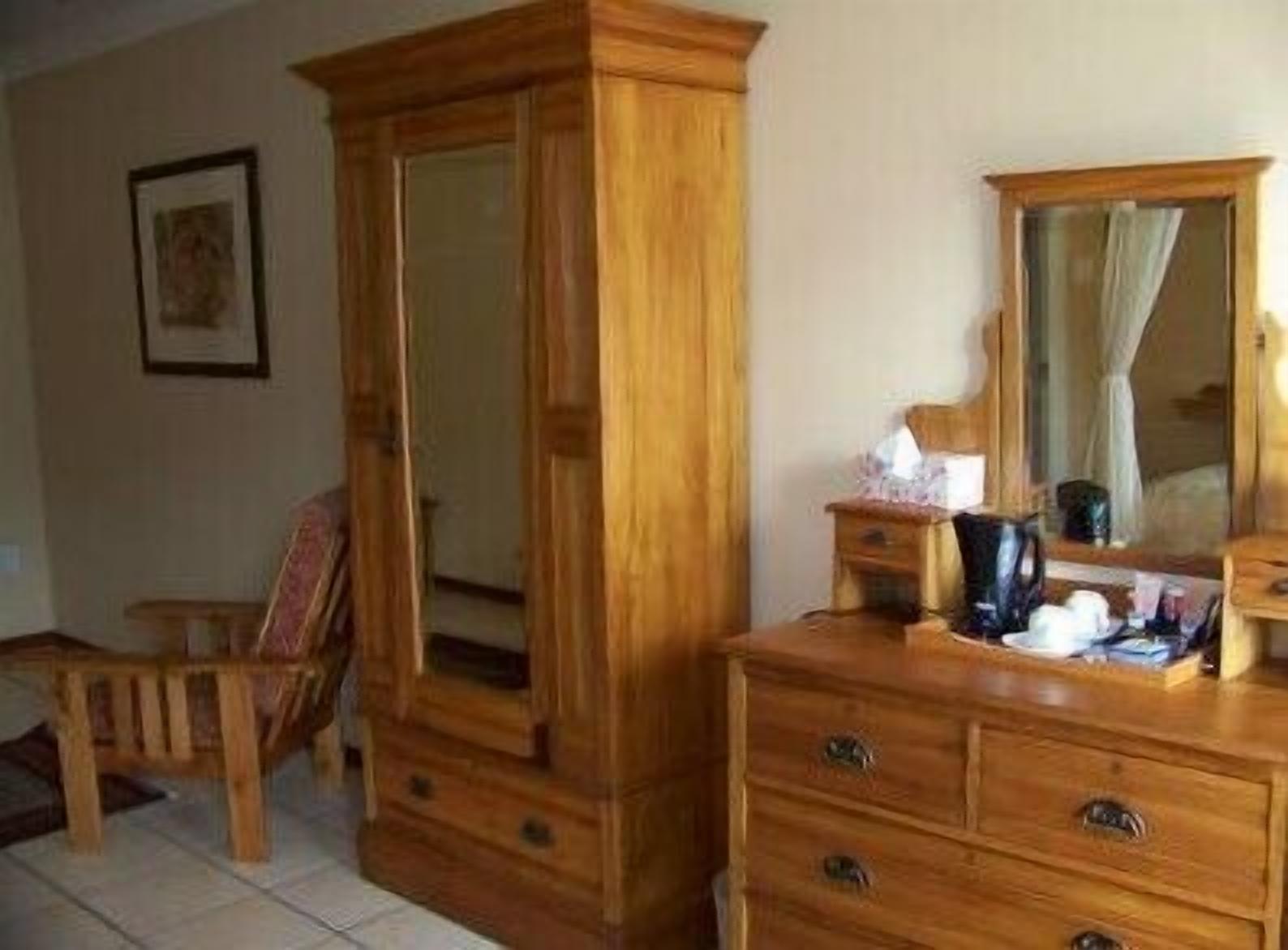 A wooden dresser with drawers and a mirror, a chair, and a small table with a coffee maker and cups.