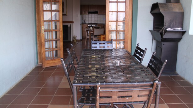 Un coin repas avec une longue table et des chaises, une cuisine à l’arrière-plan et un poêle à bois.
