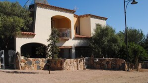 A two-story building with a stone wall entrance, a balcony, and a clear blue sky. - Antica Isola (Olbia)
