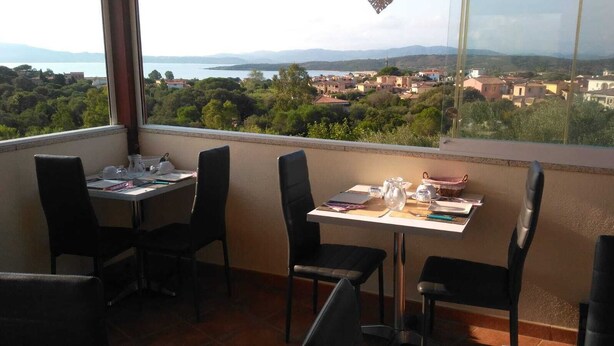 A balcony with two tables, chairs, and a view of a coastal town. - Antica Isola (Olbia)
