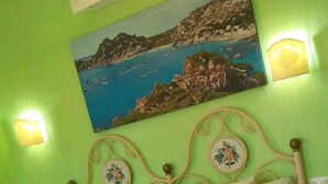 A bed with a headboard, pillows, and a blanket. There is a painting on the wall above the bed. - Antica Isola (Olbia)